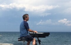 picture of Pierre playing the piano in front of the St. Lawrence river